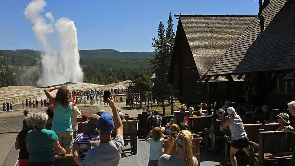 Visitors watch an Old Faithful eruption from the Old Faithful Inn porch